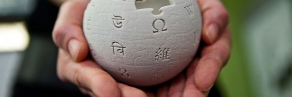 Hands are cupping a mini wikipedia globe made from wet sand