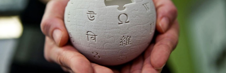 Hands are cupping a mini wikipedia globe made from wet sand