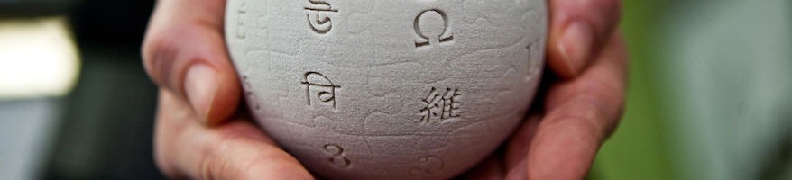 Hands are cupping a mini wikipedia globe made from wet sand