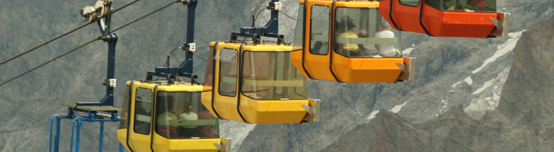 Four aerial tramway cars going up the side of a slightly snow covered mountain.