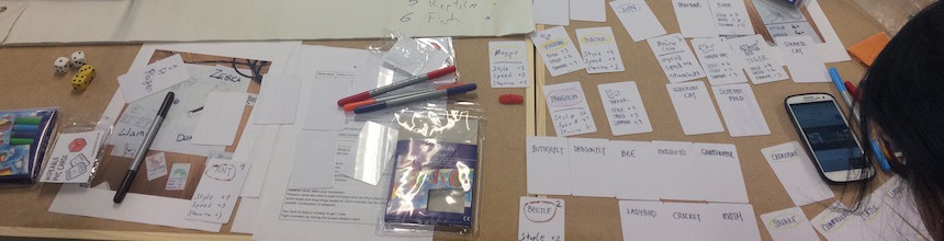 Pens, dice, cards, marker pens all strewn across a table top