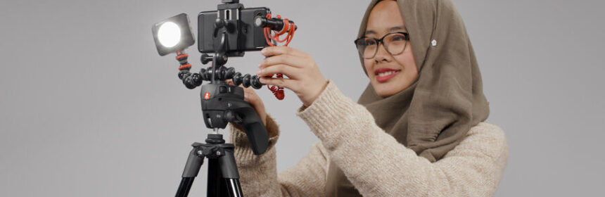 Photograph of woman wearing a headscarf and glasses, standing in front of a camera