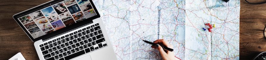 Laptop, map, and a hand holding a pen hovering over the map